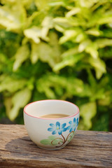 Coffee in beautifully painted coffee cup, on natural wood texture with leaves in background. Selective focus