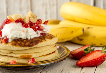 Блины с мороженным, клубникой и бананами для завтрака. Фон, текстура деревянный