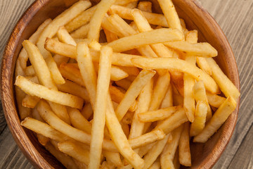 French fries in a wooden bowl, on a wooden background.