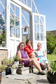 Three women sitting in front of greenhouse