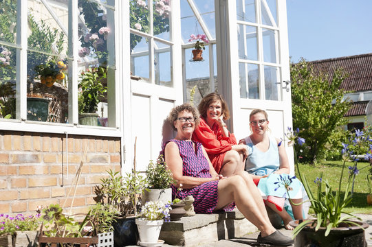 Tree women sitting on step in front of greenhouse