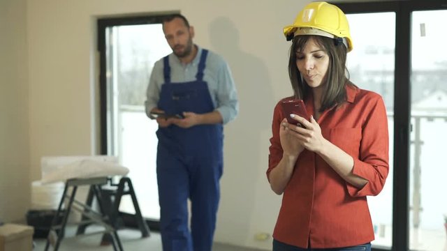 Young woman with smartphone talking to worker at her new home

