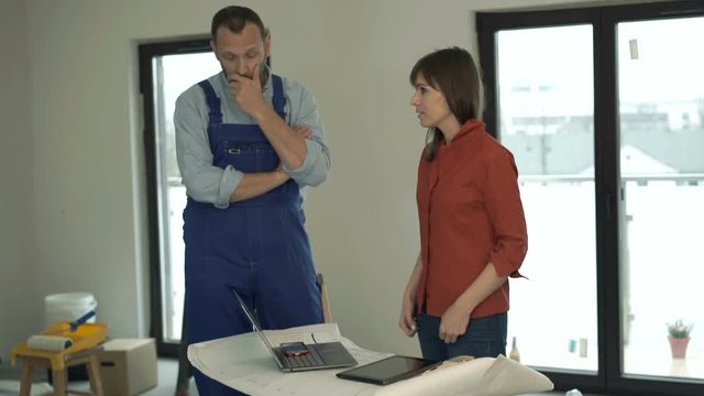 Woman with tablet and blueprints giving reprimand to male worker at her new home 
