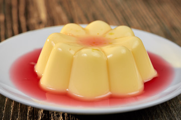 Vanilla pudding with strawberry sauce on wooden table