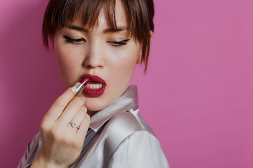 Girl beauty portrait putting red lipstick on while looking down