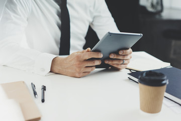 Cropped image of young businessman sitting at his office and using digital tablet, male hands searching information in internet via digital tablet in modern interior