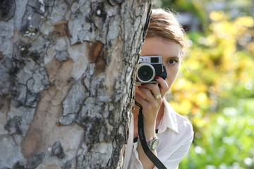Woman with camera hiding behind the tree