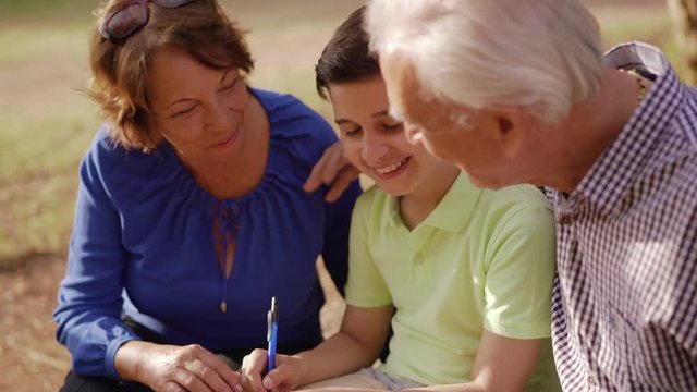 Old and young people together, seniors and children in family relationship, generations with child and elderly persons. Grandfather and grandmother helping boy with school homework, studying with book