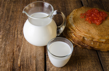 Glass jug and glass with milk on a wooden rustic background. Traditional Russian pancakes with red caviar. Maslenitsa.