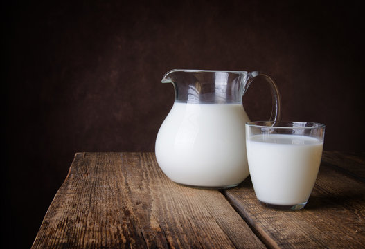 Glass jug and glass with milk on a wooden rustic background.