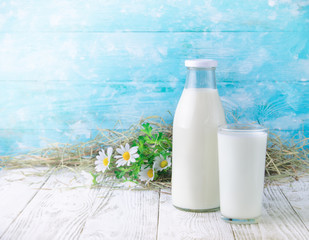 A bottle of rustic milk and glass of milk on a wooden table on blue background
