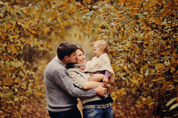 Fototapeta premium Молодые родители играют со своей маленькой дочерью в осеннем лесу