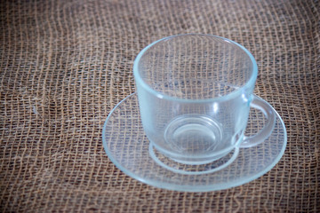 Empty glass cup standing on a table cloth surface with a saucer and spoon