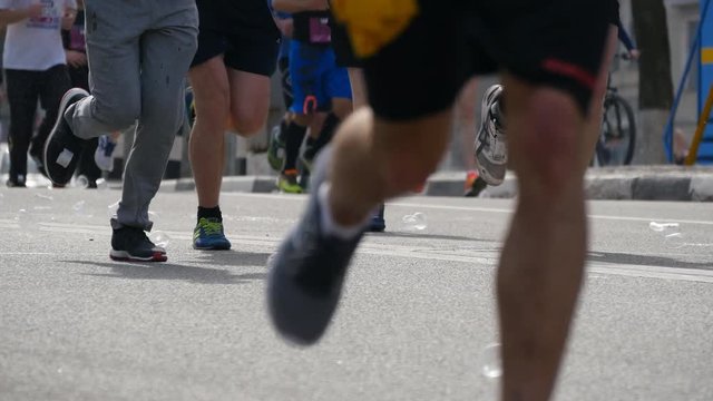 People drink the water and throw plastic cups on the street. City marathon. Feet of people. Legs of runners on the city street. Close Up 