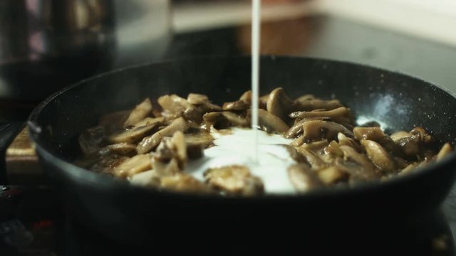Adding sour cream to frying pan with sliced mushrooms closeup