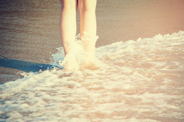 Vintage photo of woman's legs walking by sea shore.