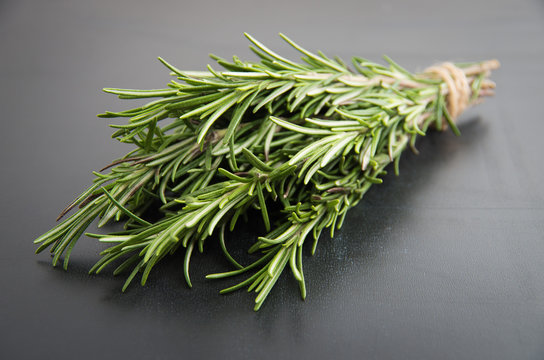 Sprigs of rosemary tied with string on a dark black background.