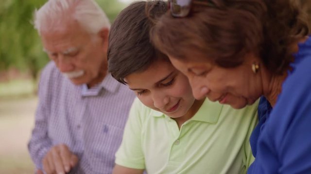 Old and young people together, seniors and children, generation gap with child and elderly persons. Boy teaching happy grandpa and grandma how to use telephone for internet, text, message. Family fun