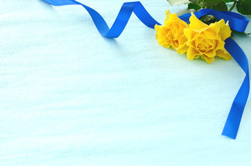 Obraz premium Żółta róża i niebieska wstążka jasnoniebieskie tło