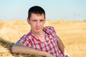 Portrait of a young man who leans on a bale of hay.