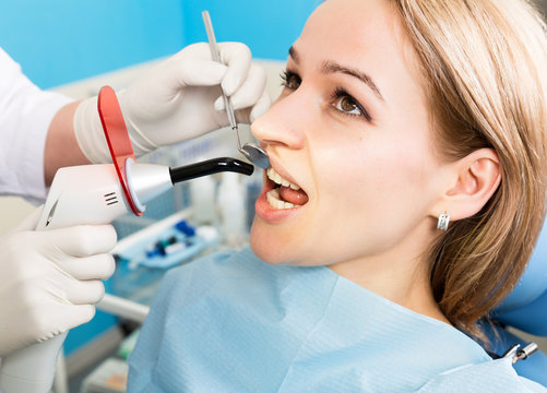 The reception was at the female dentist. Doctor examines the oral cavity on tooth decay. Caries protection. Tooth decay treatment. Dentist working with dental polymerization lamp in oral cavity