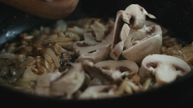 Adding sliced mushrooms to fried onions on the hot pan and stirring it closeup