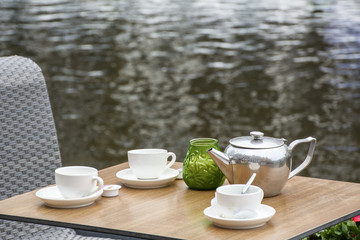Table with white cups and teapot on the street near the water