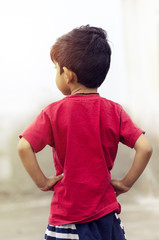 Boy child standing and waiting hands on hips rear view