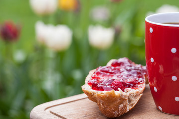 Einladung zum Frühstück im Garten, Kaffeebecher und Brötchen vor Tulpenbeet