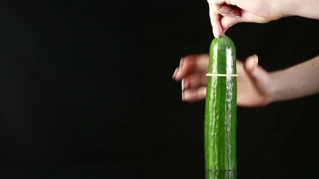 woman's hand dress the condom on cucumber