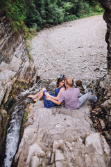 Nice couple standing near stone wall, outdoor. Beloved embracing and smiling. Woman wearing blue dress,