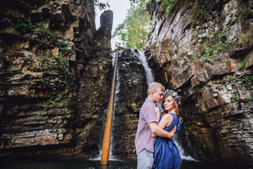 Portrait of a young couple is hugging each other near a waterfall