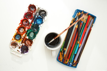 Watercolor paints in box with brush and pencils