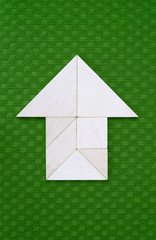 Flat lay - pictogram /symbol / icon of house or arrow showing direction made of wooden tangram pieces. Unicolor background made of green fabric texture. Vignetting. 