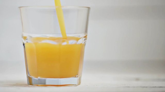 in a transparent glass on a white background pour the orange juice