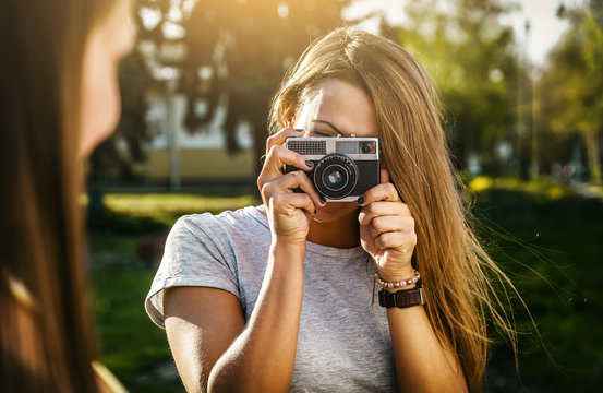 Two beautiful young women using a vintage camera in the street at summer.