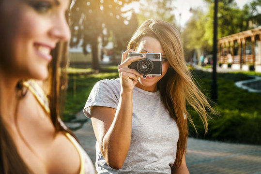 Two beautiful young women using a vintage camera in the street at summer.