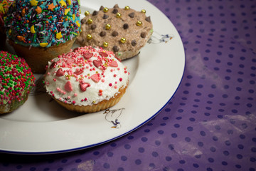Multicolored sweet cupcakes on white plate, purple background, food photo