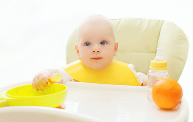 Baby sitting at the table home and eats spoon