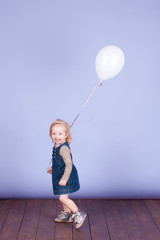 Smiling baby girl playing with balloon over blue in room. Childhood. Playful.