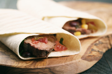 burritos with beef steak, corn, black beans and salsa sauce on wood table
