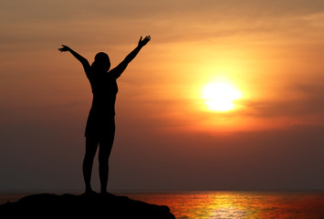 silhouette of woman with raised hands on the beach