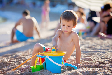Cute little preschooler boy, playing in the sand on the beach wi