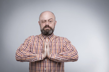 Obraz premium The bearded middle-aged man praying with hands folded, closed on