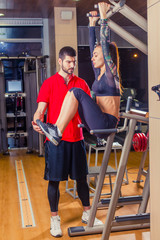 Fototapeta na wymiar fitness, sport, training and people concept - Personal trainer helping woman working with abdominal muscles press on the horizontal bar.
