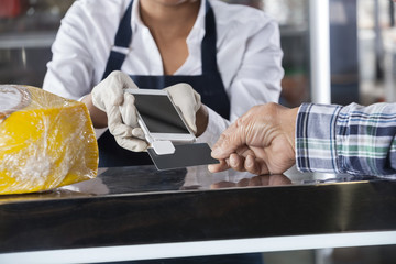 Saleswoman Accepting Payment From Customer In Cheese Shop