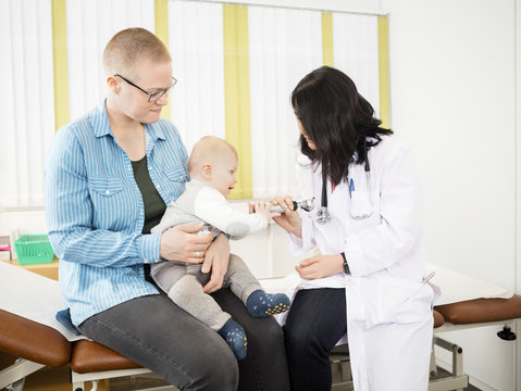 Woman Looking At Baby Grabbing Otoscope From Doctor