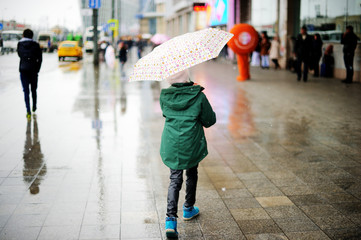 Kid girl with umbrella walking in city street