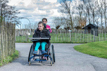 Disability a disabled child in a wheelchair / A disabled person in a wheelchair relaxing outside with her sister