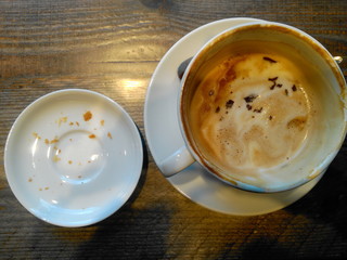 leere Kaffeetasse mit Rest Schaum und Teller mit Krümeln auf Holztisch